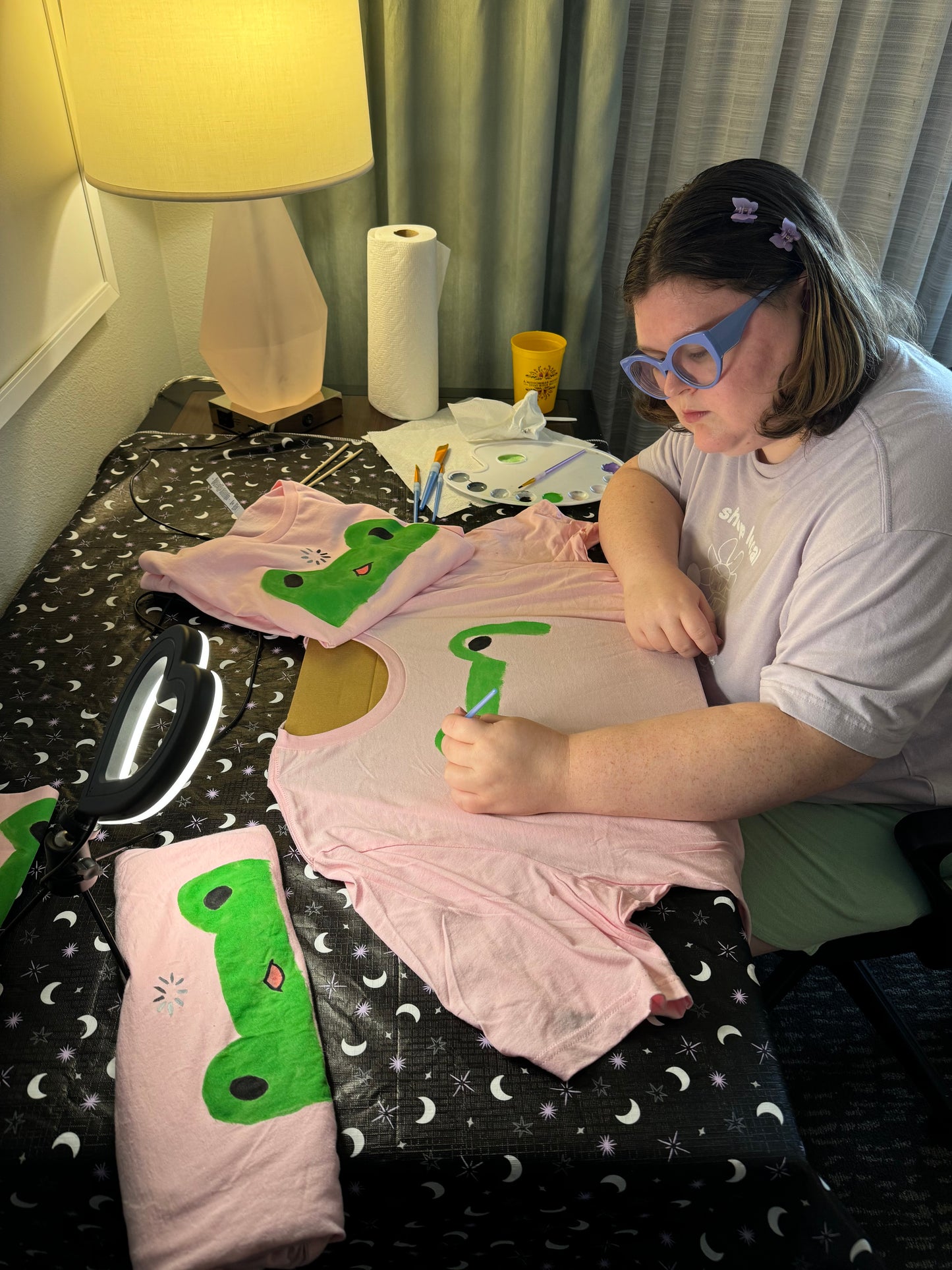 Katherine, owner of Faul Magic, a white femme presenting person hand painting one of the shirts