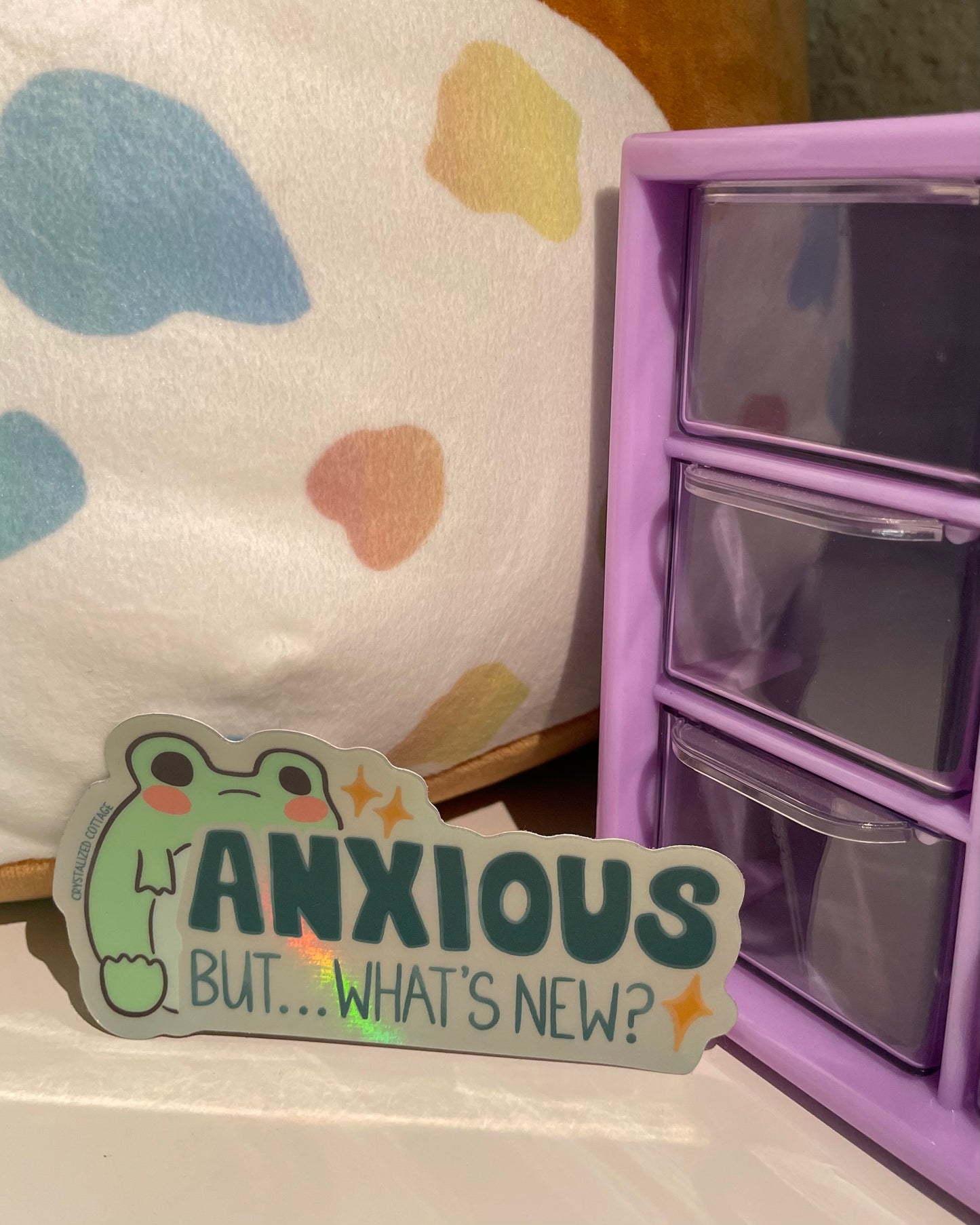 Sticker with holographic sheen and a cartoon frog says anxious but…what’s new?